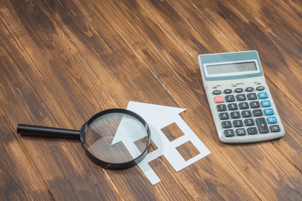 A magnified glass, paper cut out of a house and a calculator on a wooden surface